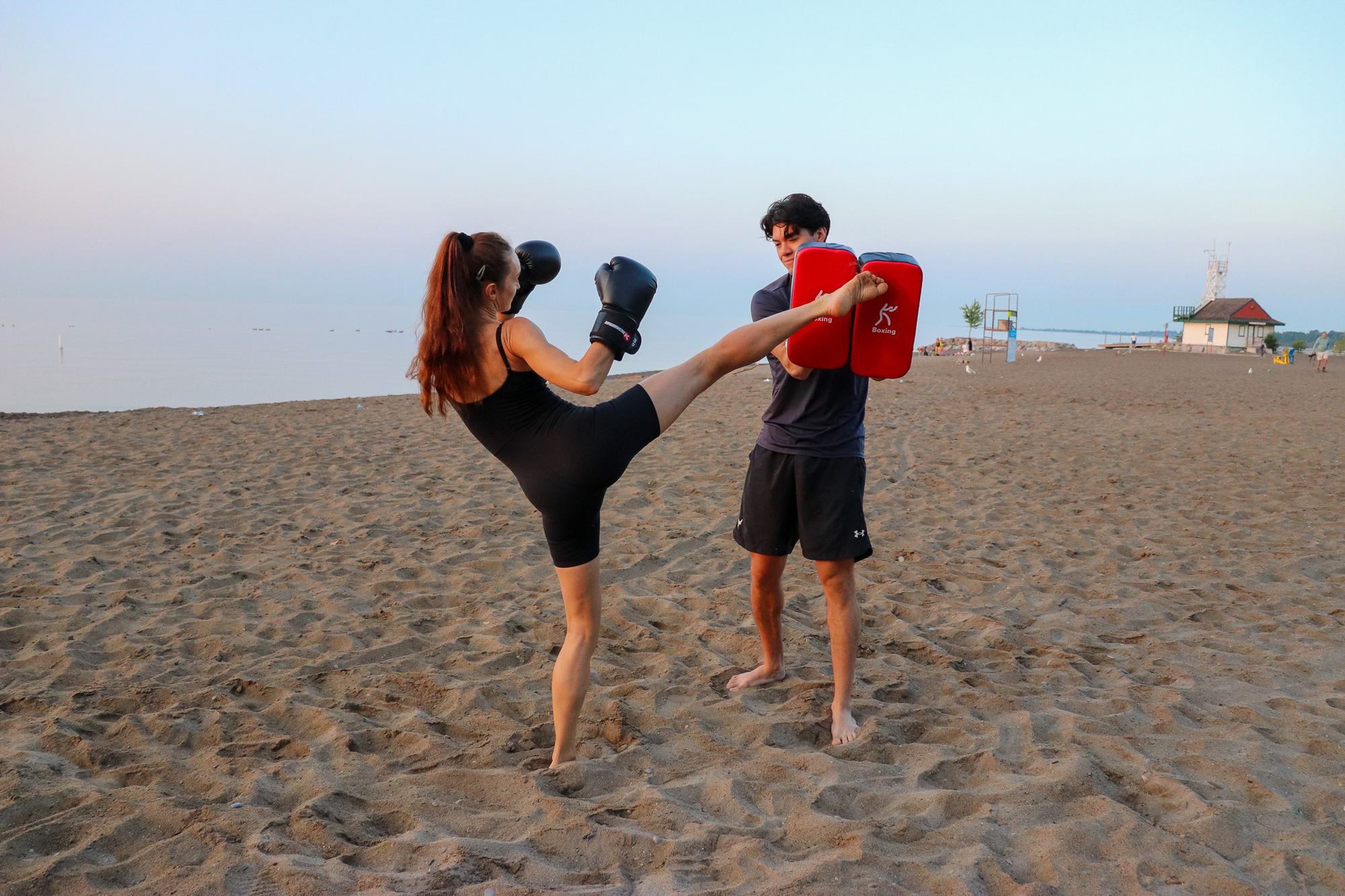 Coach Stephen holding pads for a high kick on the beach